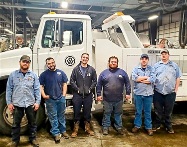A group of Fleet team members standing in front of a dump truck after completing CDL training