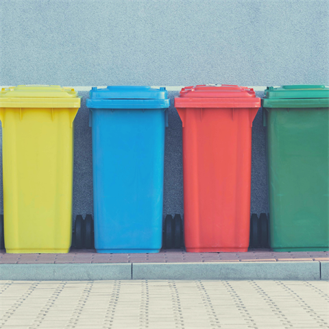 Photograph of colorful trashcans sitting next to a wall