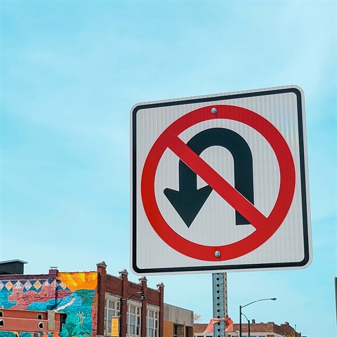 A No U-Turn sign with city buildings viewable in the background