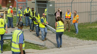 A team of several people carrying a large steel beam across a street