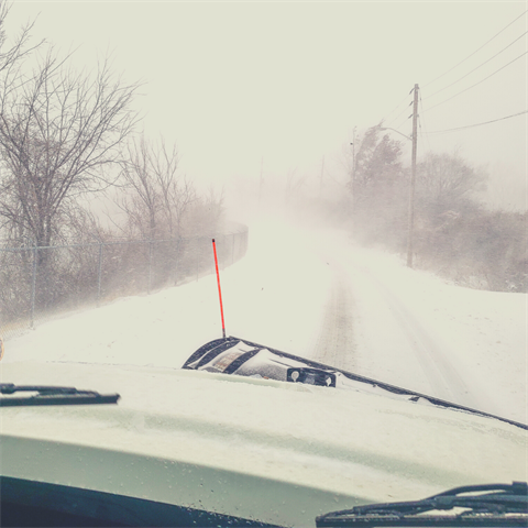 Photograph of a very snowy road from the cab of a snowplow truck