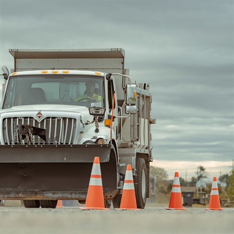 A snowplow truck navigating an obstacle course made of bright orange cones seen from ground-level.