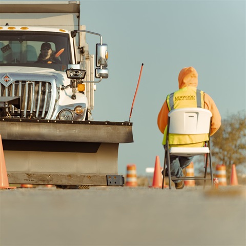 A large snowplow truck navigating an obstacle course made of cones with a person in the foreground serving as an event judge