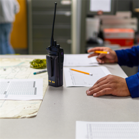 Photograph of a person standing at a table with a portable communications radio